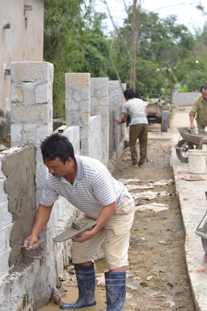 Men working on constructing a stone wall using cement in an outdoor setting.