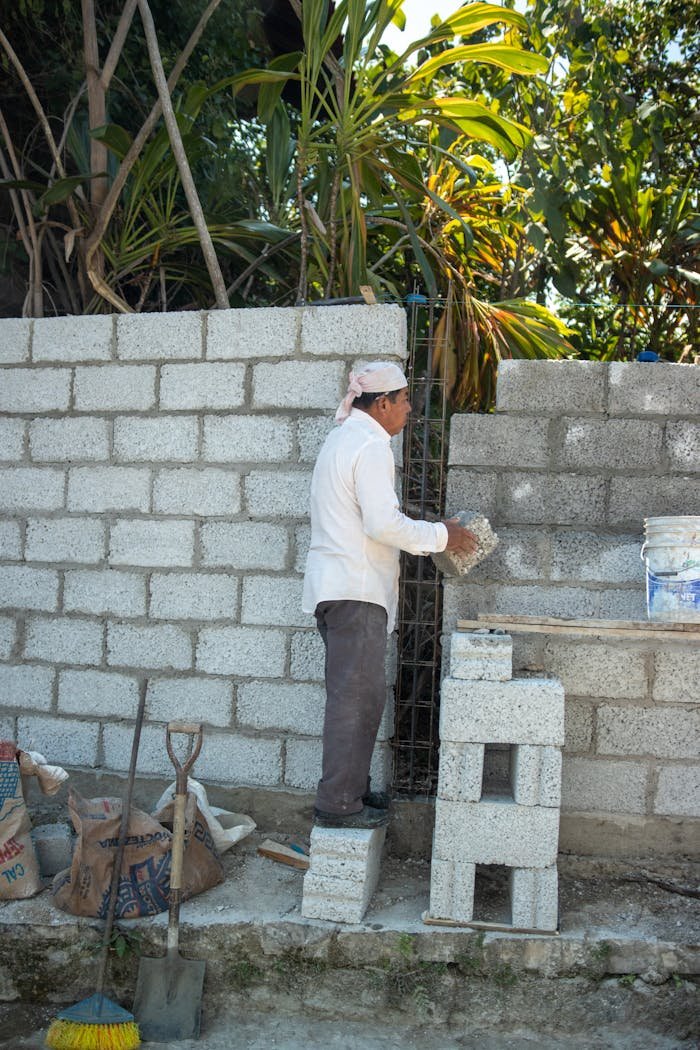 A bricklayer builds a concrete block wall outdoors, showcasing manual construction work.
