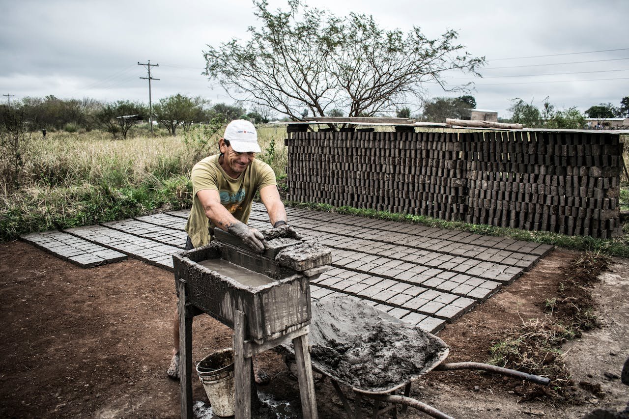 Man shaping cement bricks outdoors, showcasing traditional construction work.