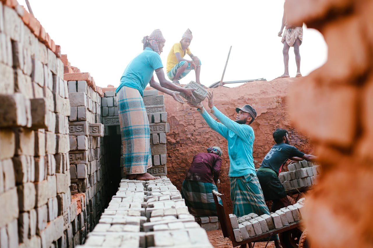 Men working together in an outdoor brickyard, moving bricks efficiently under the daylight.