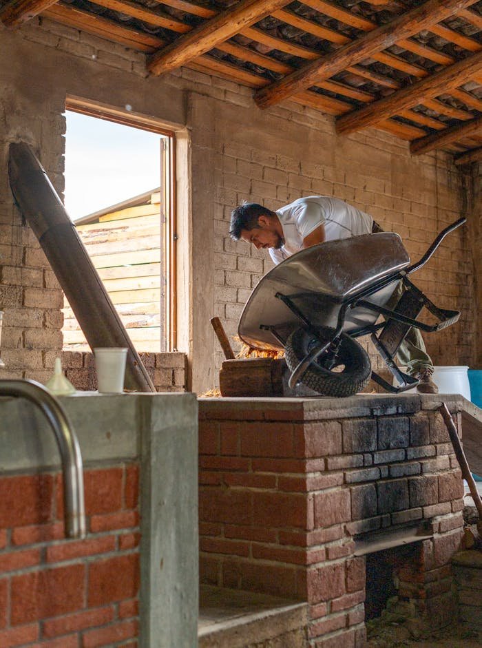 Construction worker handling a wheelbarrow indoors in a rustic brick setting.