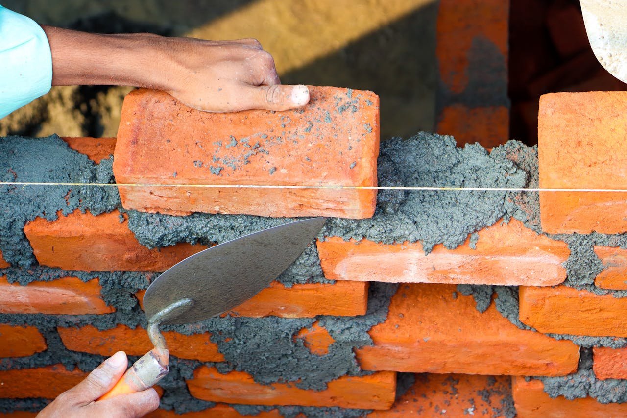 Hands laying bricks with cement in a construction setting, showcasing precise masonry work.