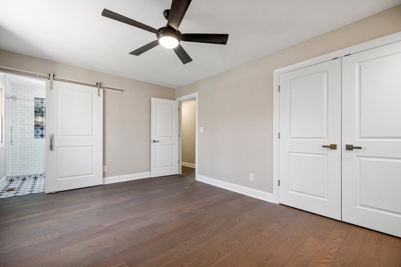 Spacious empty room with a wooden floor, ceiling fan, and sliding barn door.